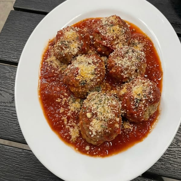 Six meatballs covered in red sauce, parmesan cheese, and herbs on a white plate.