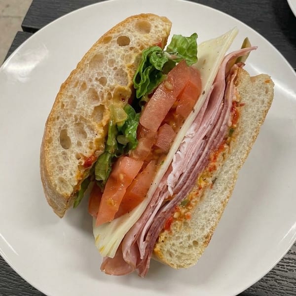 A large Italian sub sandwich with ham, cheese, lettuce, and tomatoes on a white plate.