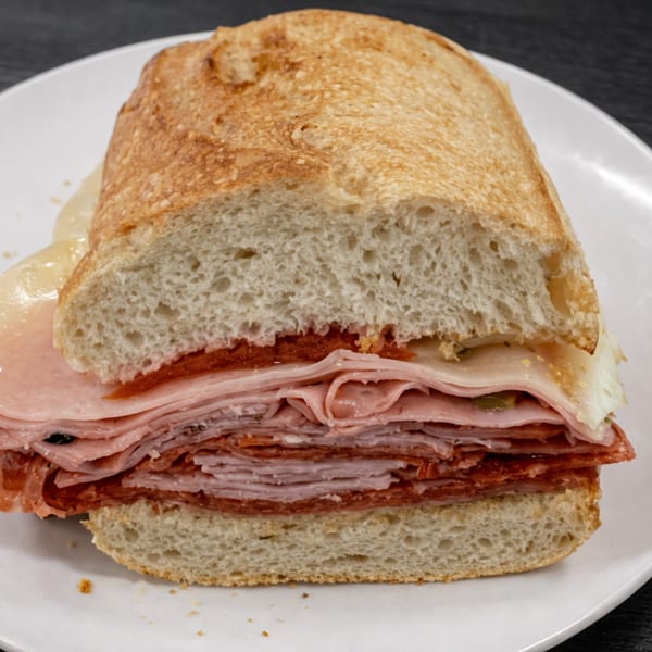 A large Italian sub sandwich, cut in half, revealing layers of deli meats and cheese on a white plate.